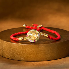 Red braided bracelet with a brass-colored rotating windmill charm