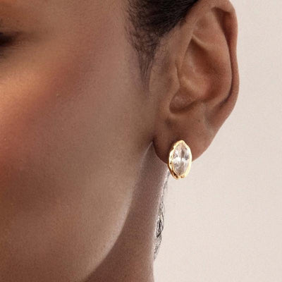 ear close-up showing the clear marquise stud and its gold-tone rim.